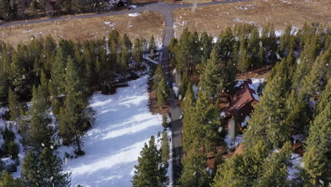 Vehicle-driving-out-of-modern-house-in-woods-during-snowfall-near-lakeside,-aerial-view
