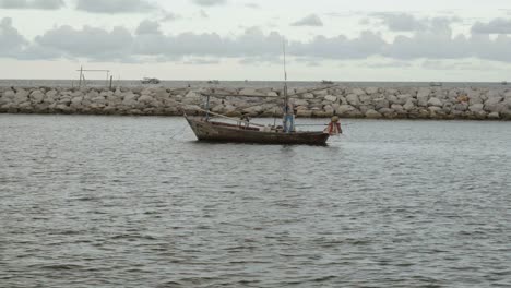 A-squid-fishing-boat-moored-in-the-marina-at-Khao-Takiab,-the-boat-protected-by-a-rocky-pier-on-a-beautiful-sunset-evening,-Hua-Hin,-Thailand