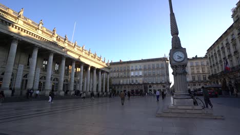 People-walking-and-skateboarding-along-the-opera-plaza-with-the-big-clock,-Wide-orbit-left-shot