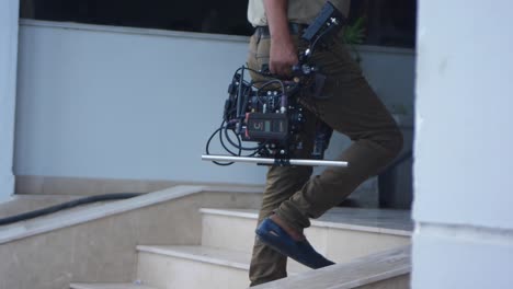 Male-Carrying-Cinema-Camera-Along-Stair-On-Film-Set-In-Karachi,-Pakistan
