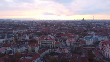 Vilnius-City,-Aerial-Cityscape,-Drone-Pullback-with-Pink-Sunset-Sky