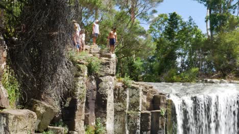 Group-of-teenager-jumping-from-cliff-of-KeriKeri-Waterfalls-into-natural-lake-during-summer