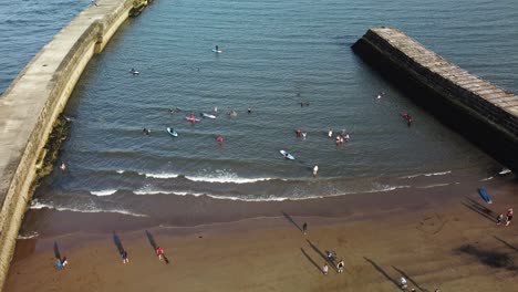 People-having-fun-in-the-sea,-aerial-descending-view-of-people-swimming-and-kayaking-in-the-sea-and-people-jogging-on-the-beach