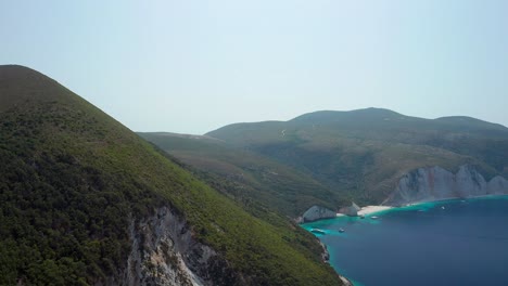 Aerial-ascending-scenic-natural-Landscape,-Fteri-beach-Surrounded-by-Green-mountain-hills