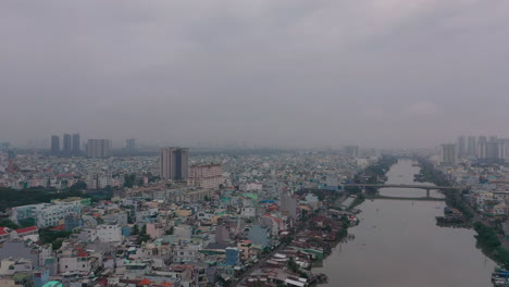 Early-foggy,smoggy-morning-drone-footage-over-canal-revealing-city-skyline-and-urban-waterfront-areas-of-Saigon,-Ho-Chi-Minh-City,-Vietnam