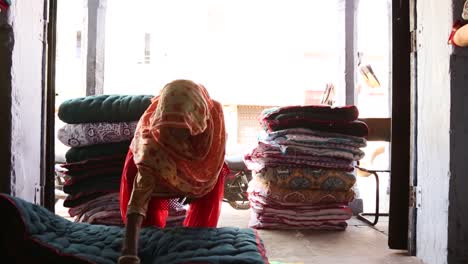 Authentic-real-life-scene-of-Indian-woman-at-work-stacking-blankets-inside-shop-in-Rajasthan,-India