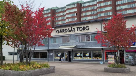 Trees-In-Autumn-Foliage-At-Gardsas-Square-In-Gothenburg,-Sweden-With-Buildings-And-Storefront-In-Background