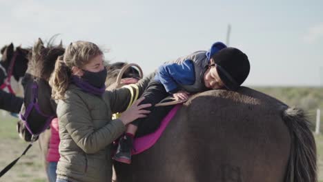 Young-Boy-Sits-Up-On-The-Top-Of-The-Horse-On-A-Windy-Weather-With-Help-Of-Female-Trainer
