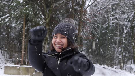 Happy-woman-smiling-and-jumping-in-forestry-area-while-snowing,-close-up-view