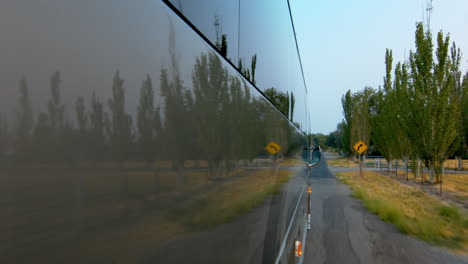 Side-view-of-a-public-bus,-shuttle,-or-school-bus-driving-and-the-road-reflection-on-it