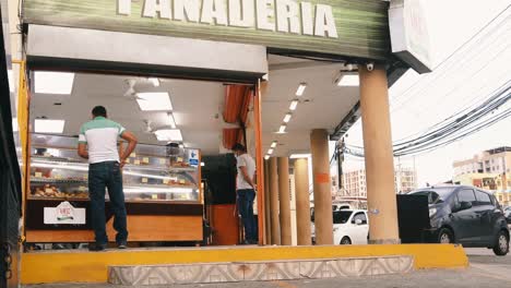 Storefront-of-a-popular-bakery-Panaderia,-2-male-customers-browse-the-assorted-selection-of-cakes-and-pastries-available-for-purchase,-Fernandez-de-Cordoba-Avenue,-Panama-City