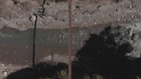 Zwei-Menschen-Gehen-über-Eine-Hängebrücke-Aus-Metalldraht,-Die-Sich-über-Einen-Felsigen-Fluss-In-Einer-Abgelegenen-Region-Der-Philippinen-Erstreckt