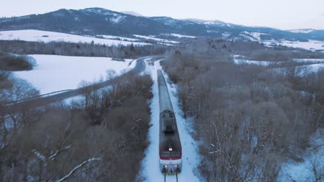 Aerial-drone-view-of-fast-moving-train-in-vast-snowy-white-landscape-scenery