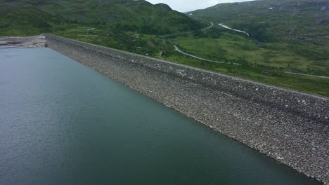 Draufsicht-Ins-Wasserreservoir-Sysendammen-Im-Norwegischen-Hardangervidda-Nationalpark-–-Luftaufnahme-Mit-Gespeichertem-Wasser-Und-Der-Spitze-Eines-Massiven-Staudamms-Mit-Der-Straße-RV7-Im-Hintergrund