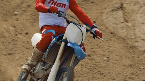 Motocross-rider-leans-over-to-take-a-turn-in-slow-motion,-comes-into-focus-and-drives-out-of-the-frame-to-the-right