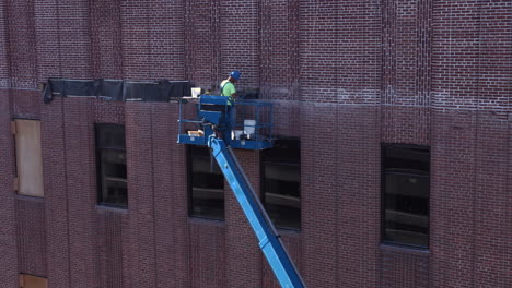 Construction-Worker-On-An-Elevated-Lift-Platform-Repairing-Exterior-Brick-Wall-Of-A-Building