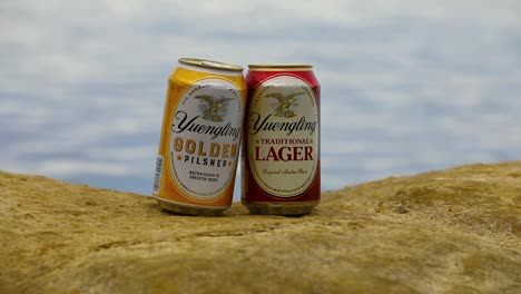 This-is-a-static-shot-of-Yuengling-Traditional-Lager-and-Golden-Pilsner-beer-cans-on-a-rock-by-the-lake