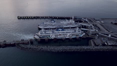 Two-BCferries-ferries-docked-at-Tsawwassen-Vancouver-ferry-terminal-at-sunset,-Aerial-tilt-up-reveal