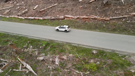 A-lone-white-Subaru-Crosstrek-driving-through-a-clear-cut-forest-area,-aerial-track,-Illustrative-Editorial