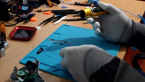 Gloved-Hands-Of-Technician-Applying-Insulation-Gel-On-Battery-Wires-Indoors-On-Workbench