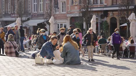 Two-female-friends-eating-Belgian-Fries-at-Oude-Markt-against-crowd-of-students-at-open-air-cafes---Leuven,-Belgium