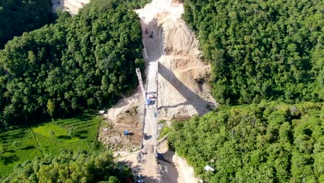 Heavy-equipment-building-bridge-over-valley-in-Indonesia-forest-area,-aerial-view
