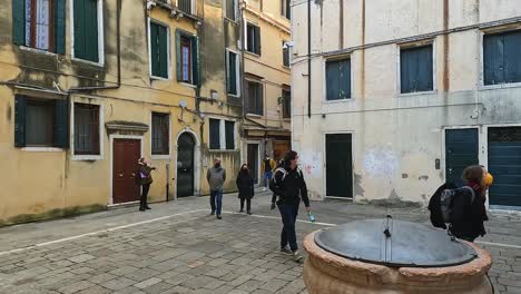 Tourists-walk-in-a-small-square-with-ancient-well-of-the-Jewish-Ghetto-of-Cannaregio-in-Venice,-Italy