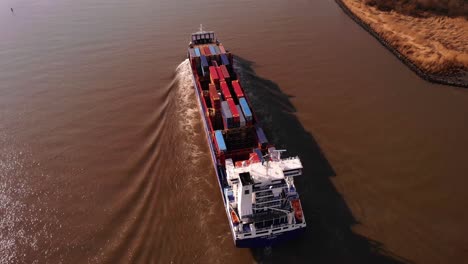 Aerial-Over-Stern-Of-WEC-de-Hoogh-Cargo-Ship-Navigating-Along-Oude-Maas