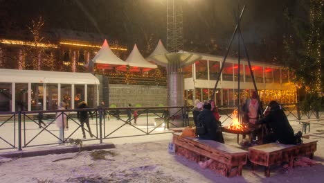 Gente-Patinando-En-La-Pista-De-Hielo-Durante-Las-Vacaciones-De-Navidad-Cerca-De-Una-Fogata-Durante-El-Invierno-En-Oslo,-Noruega