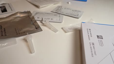 Table-filled-with-waste-from-antigen-testing-procedures---Used-disposable-covid-testing-equipment-on-white-surface---Closeup-sliding-left-to-right