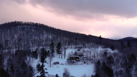 Cabin-with-barn-nestled-in-snowy-mountains-of-Vermont-during-colorful-sunset