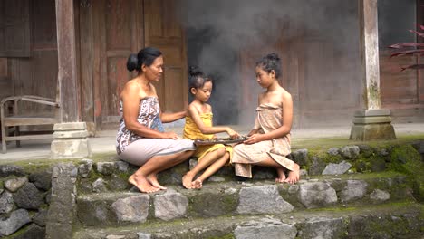 two-daughters-and-a-mother-accompanying-her-child-to-play-Dakon,-a-traditional-Javanese-game-on-the-terrace-of-the-house