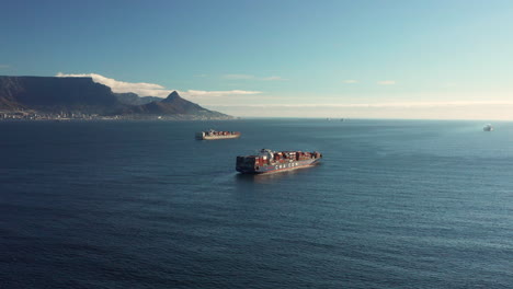 Cargo-Ship-With-Intermodal-Containers-Sailing-In-The-Ocean-With-Table-Mountain-In-The-Background-Seen-From-Blouberg,-South-Africa