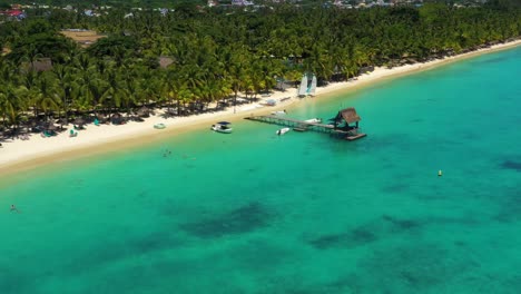 Glide-above-a-sunny-pier-and-crystal-clear-ocean-at-Trou-aux-Biches,-Mauritius
