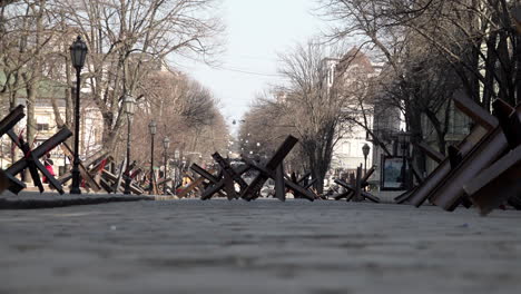 La-Gente-Pasa-Por-Trampas-De-Tanques-Hechas-De-Vigas-De-Metal-De-Acero-Soldadas-En-Una-Calle-Adoquinada-Durante-La-Invasión-Rusa-De-Ucrania