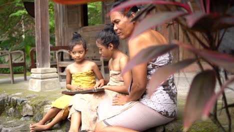 two-daughters-and-a-mother-accompanying-her-child-to-play-Dakon,-a-traditional-Javanese-game-on-the-terrace-of-the-house