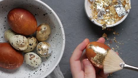 Close-up-shot-of-a-female-hand-removing-golden-foil-from-orange-colored-painted-Easter-egg