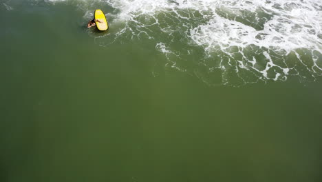 Static-aerial-birdseye-shot-of-woman-with-yellow-surfboard-riding-against-wave