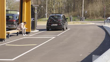 A-lone-man-patiently-waits-at-a-charging-station-for-his-electric-vehicle-to-charge