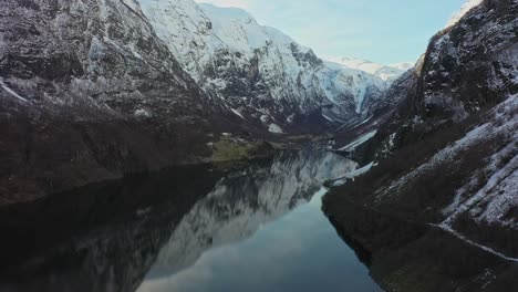 Beautiful-aerial-flying-in-unesco-listed-Naeroyfjord-towards-Gudvangen---Snow-capped-tall-mountains-and-mirror-like-reflections-in-water-surface
