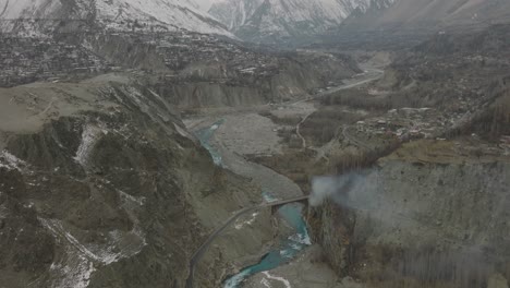 Antena-Sobre-El-Río-De-Color-Turquesa-En-El-Valle-De-Hunza-Con-Humo-Que-Se-Eleva-Cerca-Del-Puente