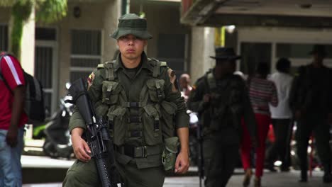 Ein-Junger-Kolumbianischer-Militärmann-Hält-Ein-Gewehr-In-Der-Hand-Und-Hält-Auf-Einer-Belebten-Straße-Ausschau-Zwischen-Zivilisten