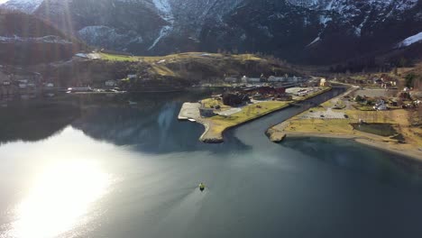 Flam-and-Aurlandsfjord-beautiful-aerial-view-with-sunrays-from-top-left-corner-and-bright-reflections-in-sea---Norway-descending-and-approaching-aerial-during-spring