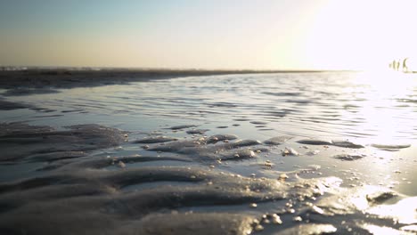 Makroaufnahme-Von-Schaum-Auf-Dem-Sand-Mit-Ruhiger-Meereslandschaft-Im-Hintergrund-Bei-Sonnenaufgang
