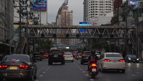 Coches-Y-Scooters-Conduciendo-Por-La-Concurrida-Calle-Phetchaburi-En-El-Centro-De-La-Ciudad-De-Bangkok-Al-Atardecer,-Conduciendo-Por-La-Concurrida-Calle-De-Bangkok-Durante-La-Hora-Azul