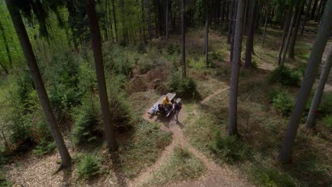 Aerial-drone-rotating-shot-of-a-couple-taking-rest-on-a-wooden-bench-while-hiking-through-green-forest-in-Hřebeč,-Czech-Republic-at-daytime