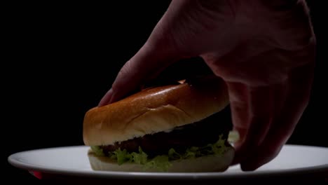 Aufnahmen-Eines-Köstlichen-Burgers,-Der-Von-Einem-Teller-Mit-Schwarzem-Hintergrund-Genommen-Wird