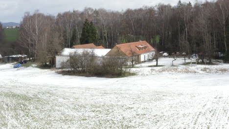 Farmhouse-with-snowy-fields-and-leafless-trees-in-winter-countryside