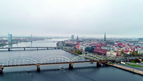 Aerial-drone-shot-flying-over-the-bridges-over-river-Daugava-with-Riga-old-town-in-the-background-on-a-cloudy-day-in-Riga,-Latvia