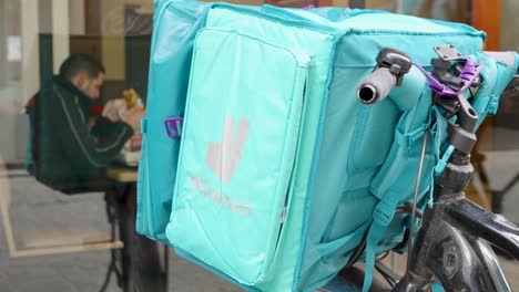 Deliveroo-food-bag-against-male-rider-eating-a-burger-in-the-restaurant-during-his-break-in-Brussels,-Belgium